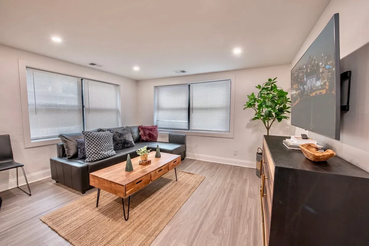 A spacious living room featuring a comfortable sofa, stylish coffee table, lush green plant, and a flat-screen TV. Natural light fills the room, accentuating the modern decor and open, welcoming layout, perfect for relaxing or socializing.