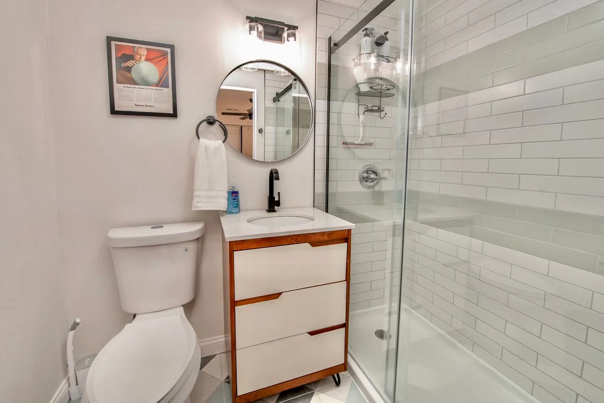 A bright, contemporary bathroom showcasing a modern sink, large mirror, glass-enclosed shower, quality fixtures, and tasteful wall art. The space feels fresh and inviting, ideal for daily self-care routines.