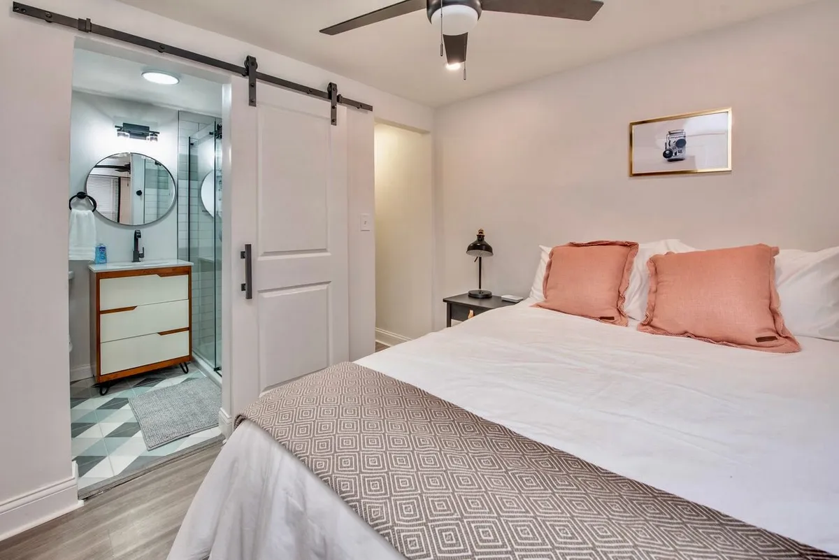 A stylish bedroom with decorative pillows atop the bed, a sliding barn door, and an open view into the adjoining bathroom. The room feels both cozy and modern, inviting you to unwind and seamlessly connecting the bedroom retreat to the luxurious bath.