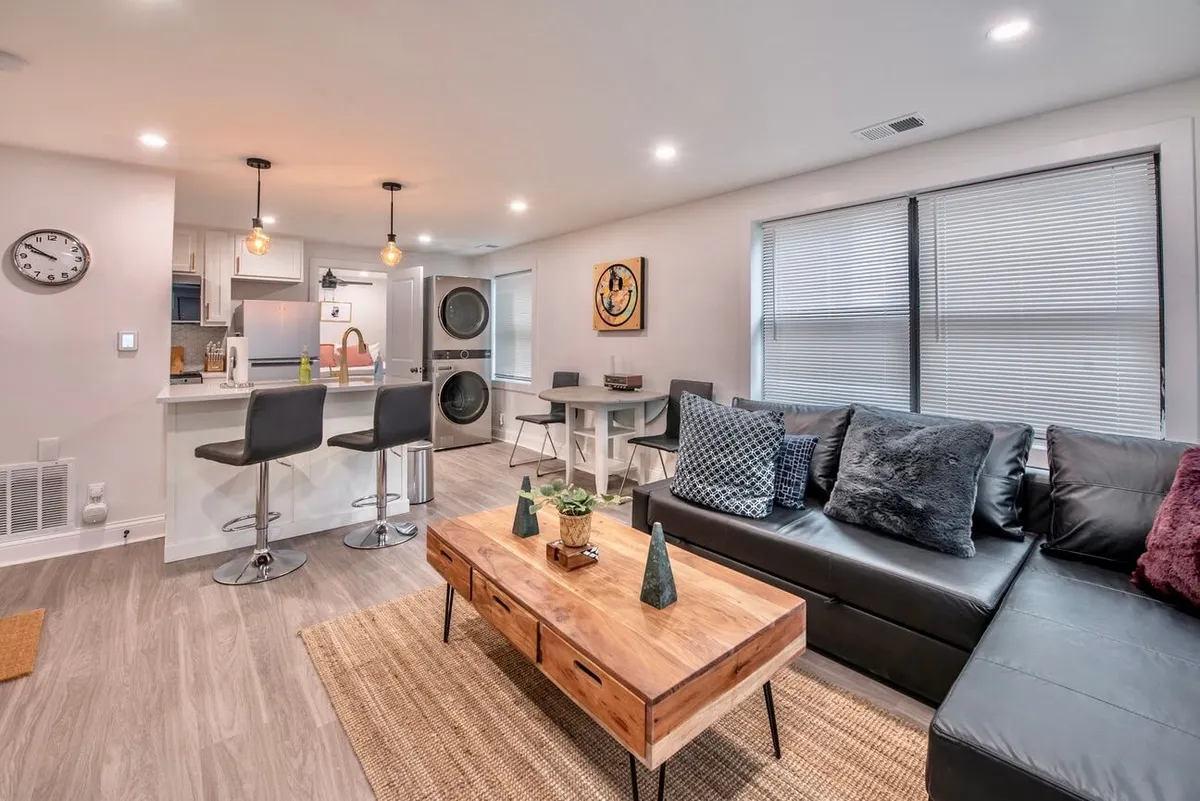 A modern living area with a wooden coffee table, black leather sofa, elegant pendant lighting, and wall art. The arrangement invites conversation or quiet moments, and the decor blends sleek, contemporary finishes with cozy touches.