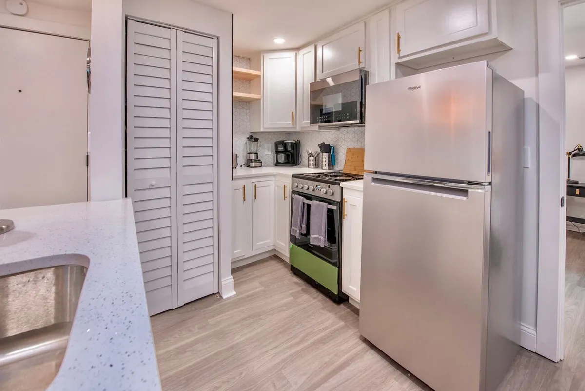 This image features a bright, modern kitchen with a green stove, sleek white cabinetry, expansive countertops, and visible kitchen appliances. The scene conveys a space designed for both cooking and socializing, with a clean, open feel and contemporary finishes.